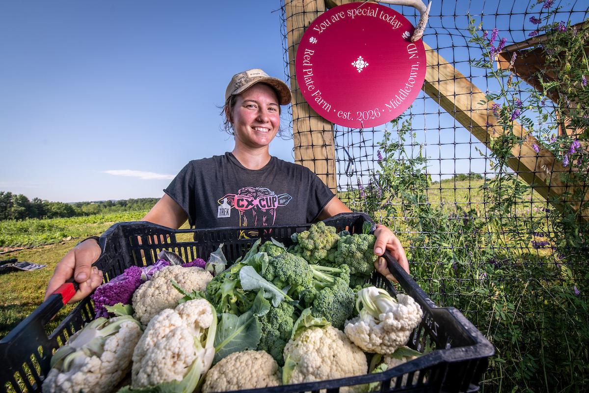 This is a photo of a female farmer holding out a variety of vegetables in a basket